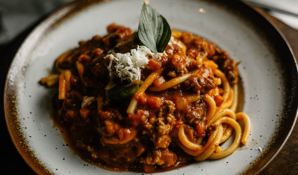 A close-up of flavorful Italian pasta with rich meat sauce garnished with basil and cheese.