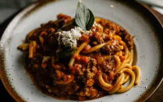 A close-up of flavorful Italian pasta with rich meat sauce garnished with basil and cheese.