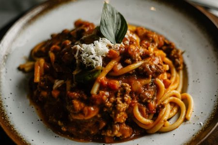A close-up of flavorful Italian pasta with rich meat sauce garnished with basil and cheese.