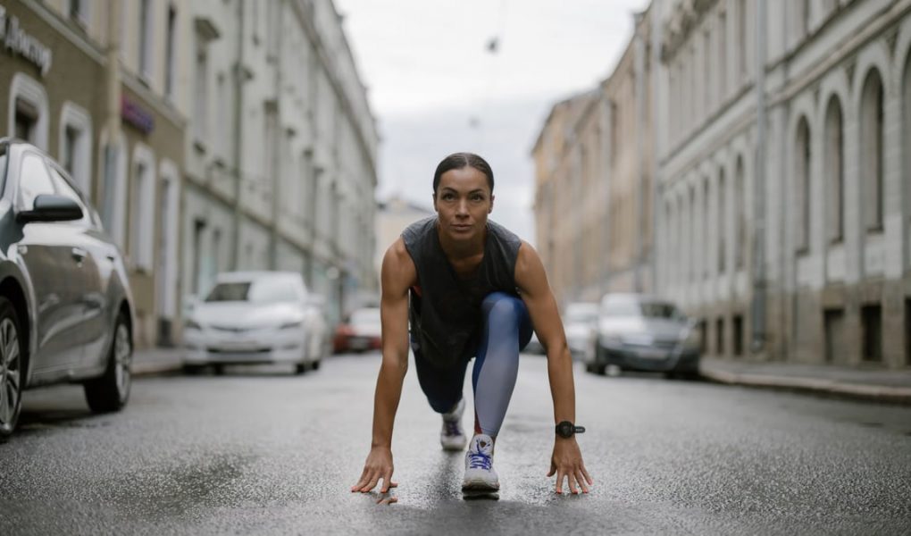 Woman in activewear poised for a run on a city street, symbolizing fitness and determination.