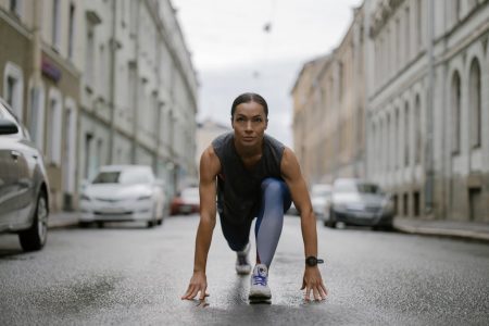 Woman in activewear poised for a run on a city street, symbolizing fitness and determination.
